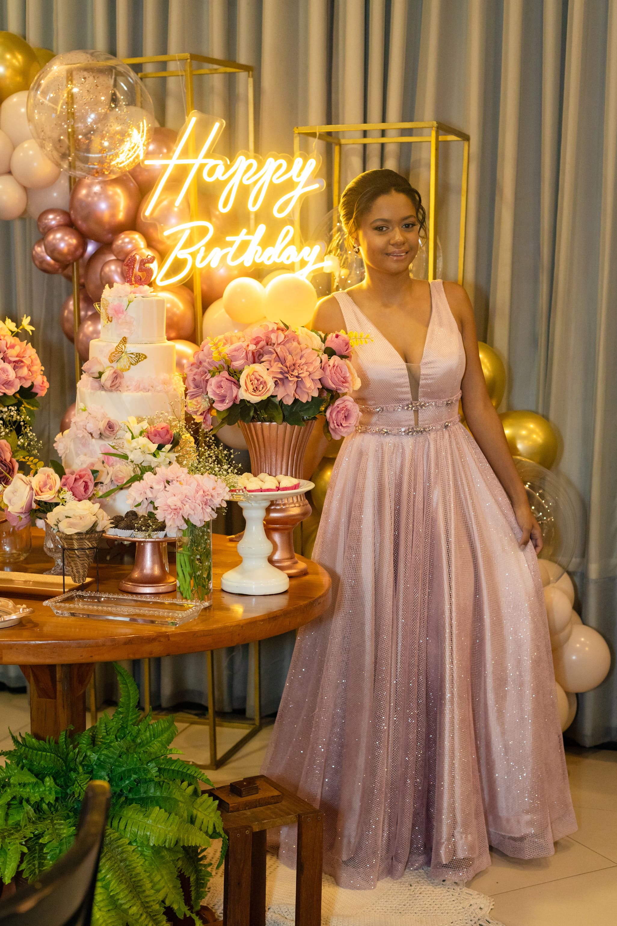 Anna Julia com vestido rosa ao lado da mesa de decoração na festa de debutante