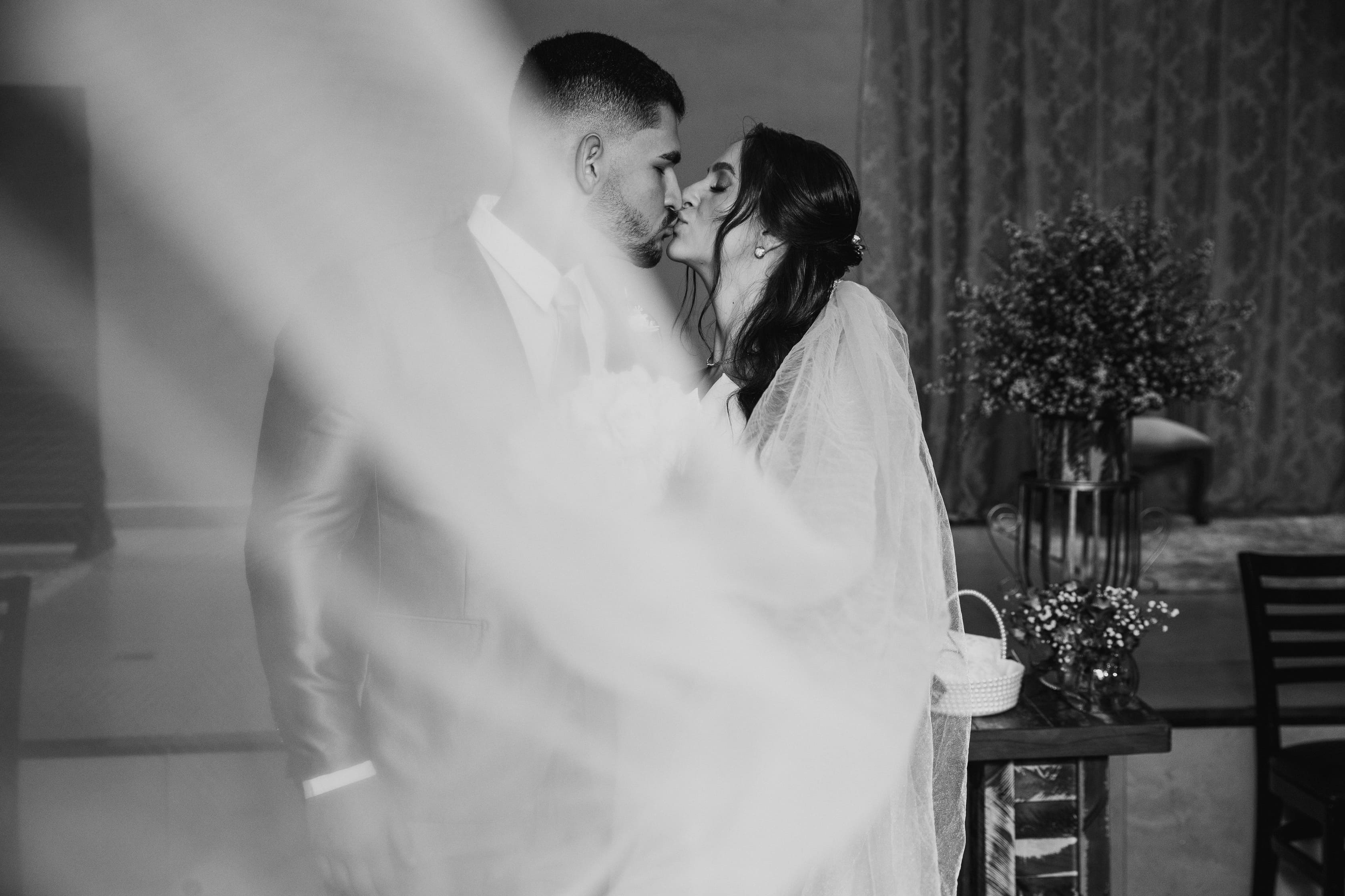 Beijo artístico do casal com véu esvoaçante em preto e branco