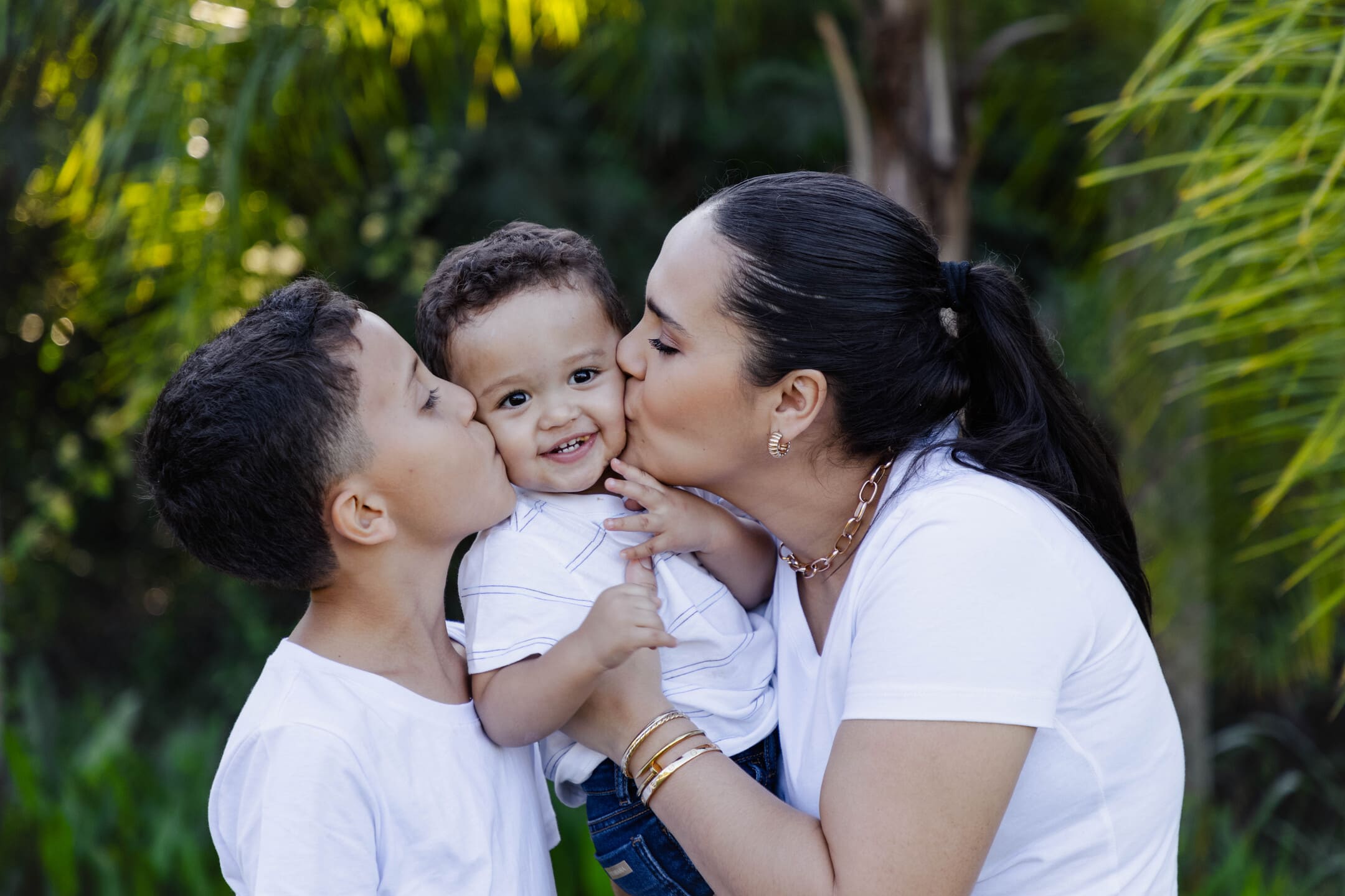 Miguel e Géssica beijando Théo em momento de carinho no ensaio de família no Forest Hill Cianorte