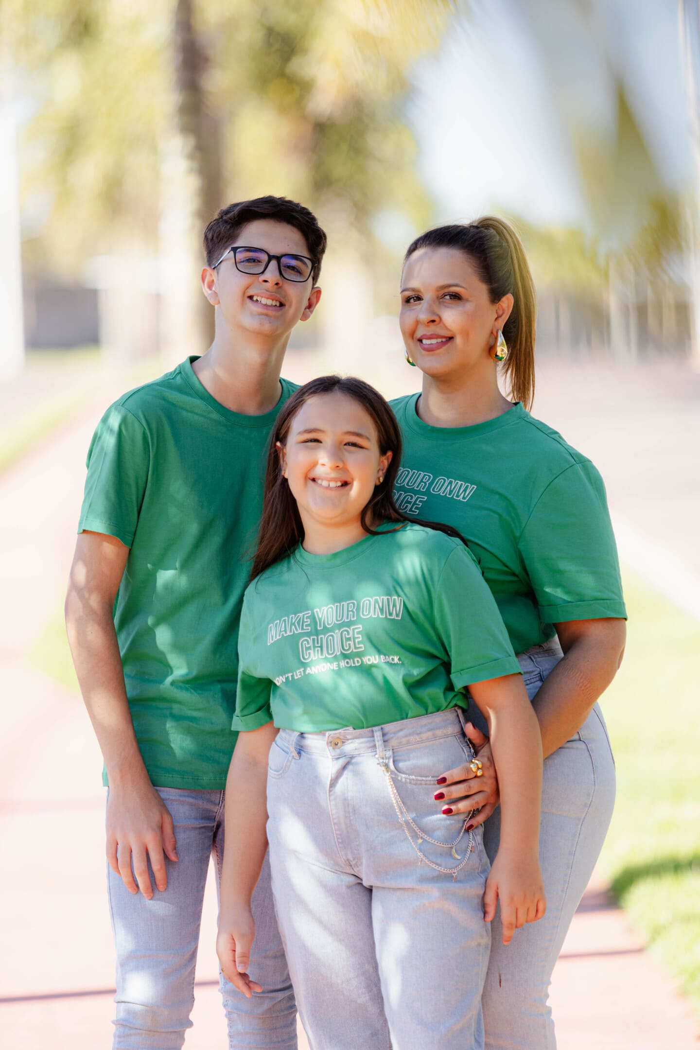 Meire, Vinícius e Maria Fernanda de camisetas verdes combinando no caminho de palmeiras do Forest Hill
