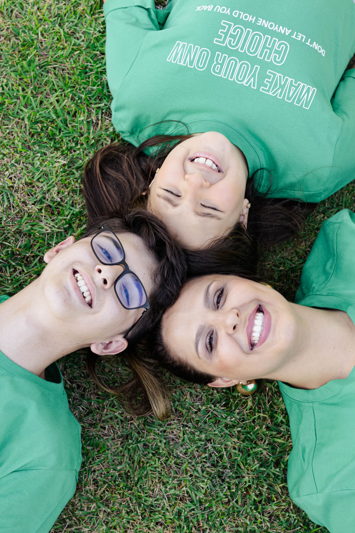 Meire, Vinícius e Maria Fernanda deitados no gramado sorrindo vistos de cima no Forest Hill Cianorte