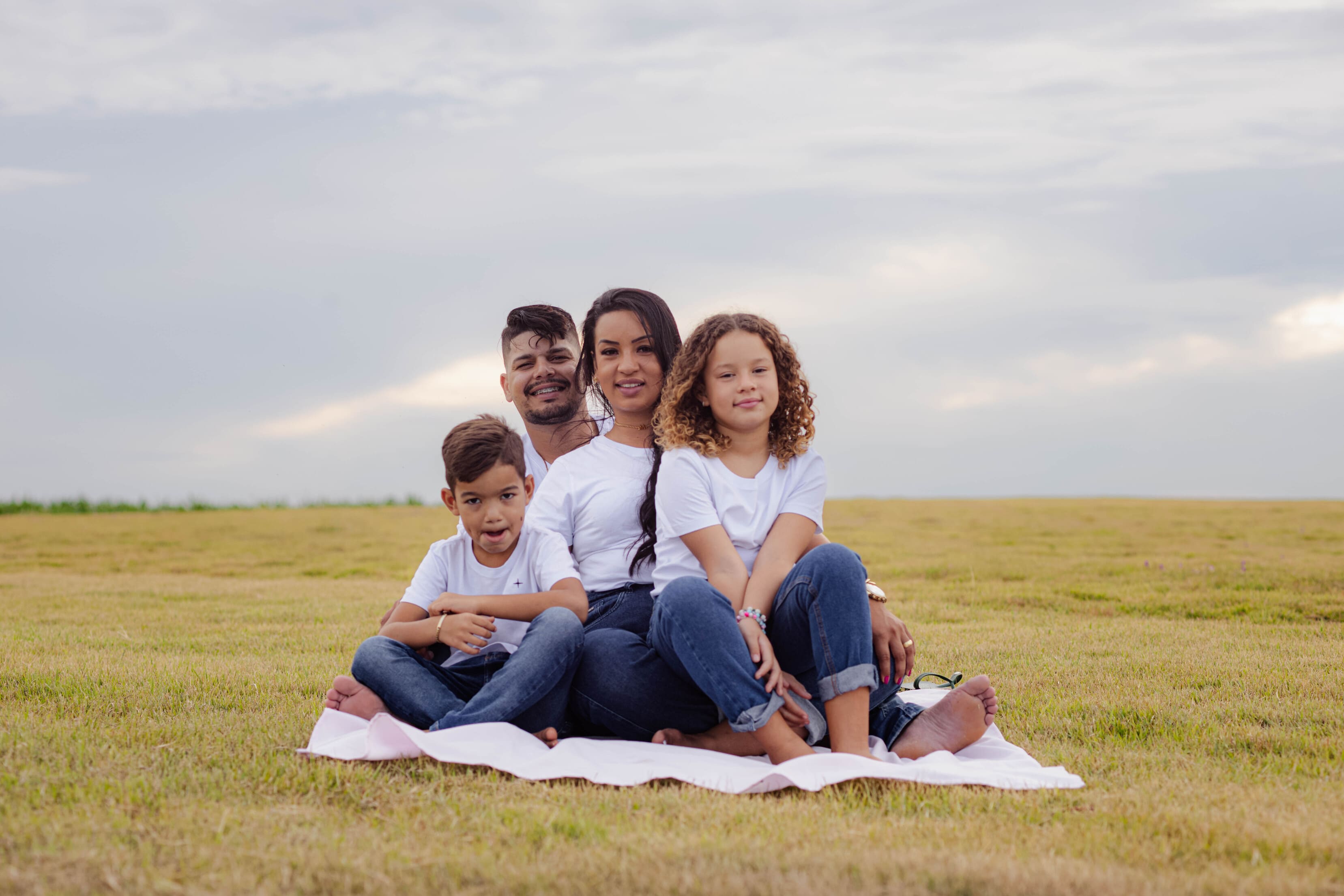 Família completa caminhando de mãos dadas no gramado de Vidigal durante o pôr do sol em Cianorte