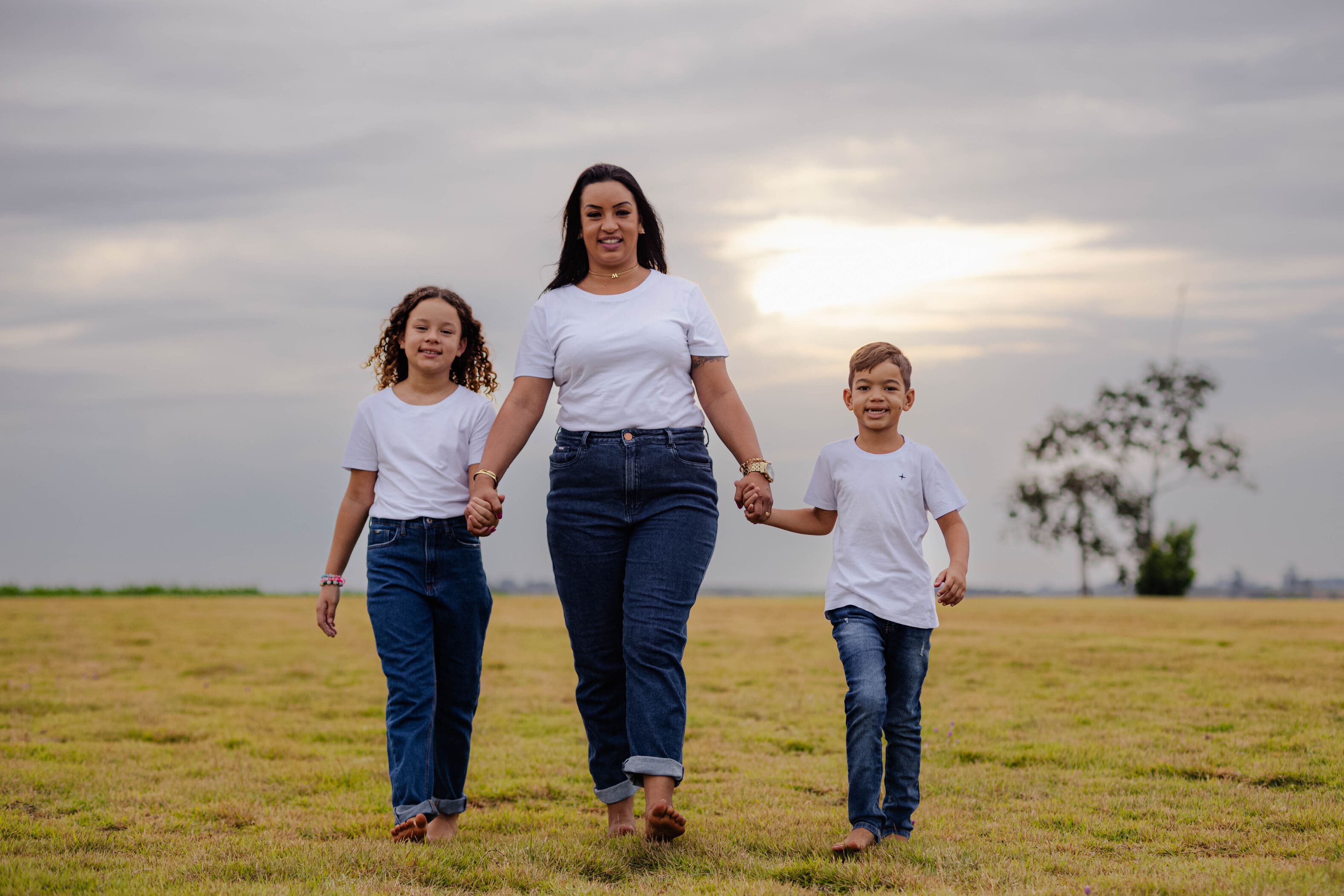 Wanessa caminhando de mãos dadas com Ana Laura e Lorenzzo no entardecer nublado em Vidigal