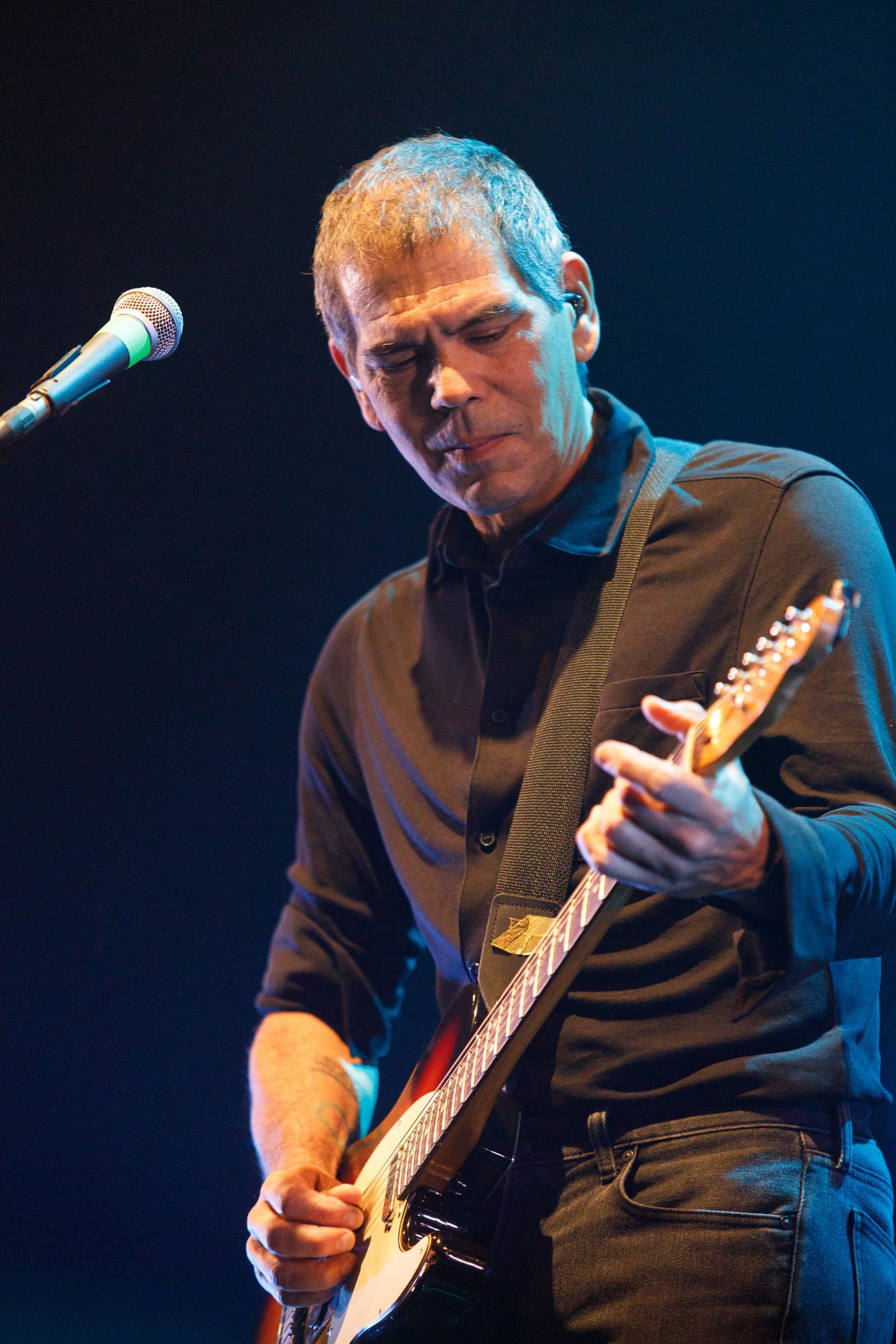 Dado Villa-Lobos tocando guitarra com iluminação azul no show da turnê As V Estações em Maringá