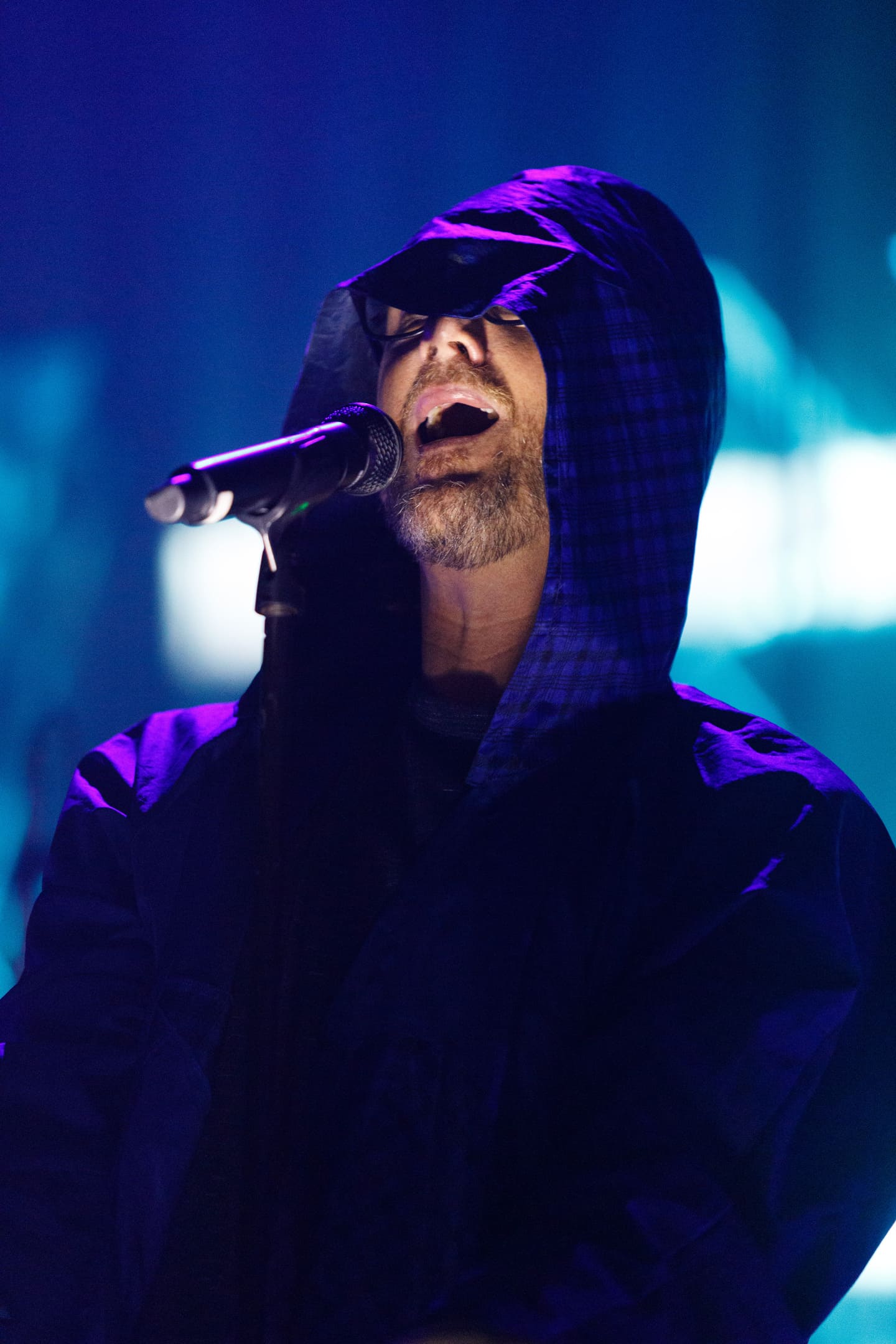 Vocalista cantando com capuz e iluminação roxa no show As V Estações da Legião Urbana em Maringá